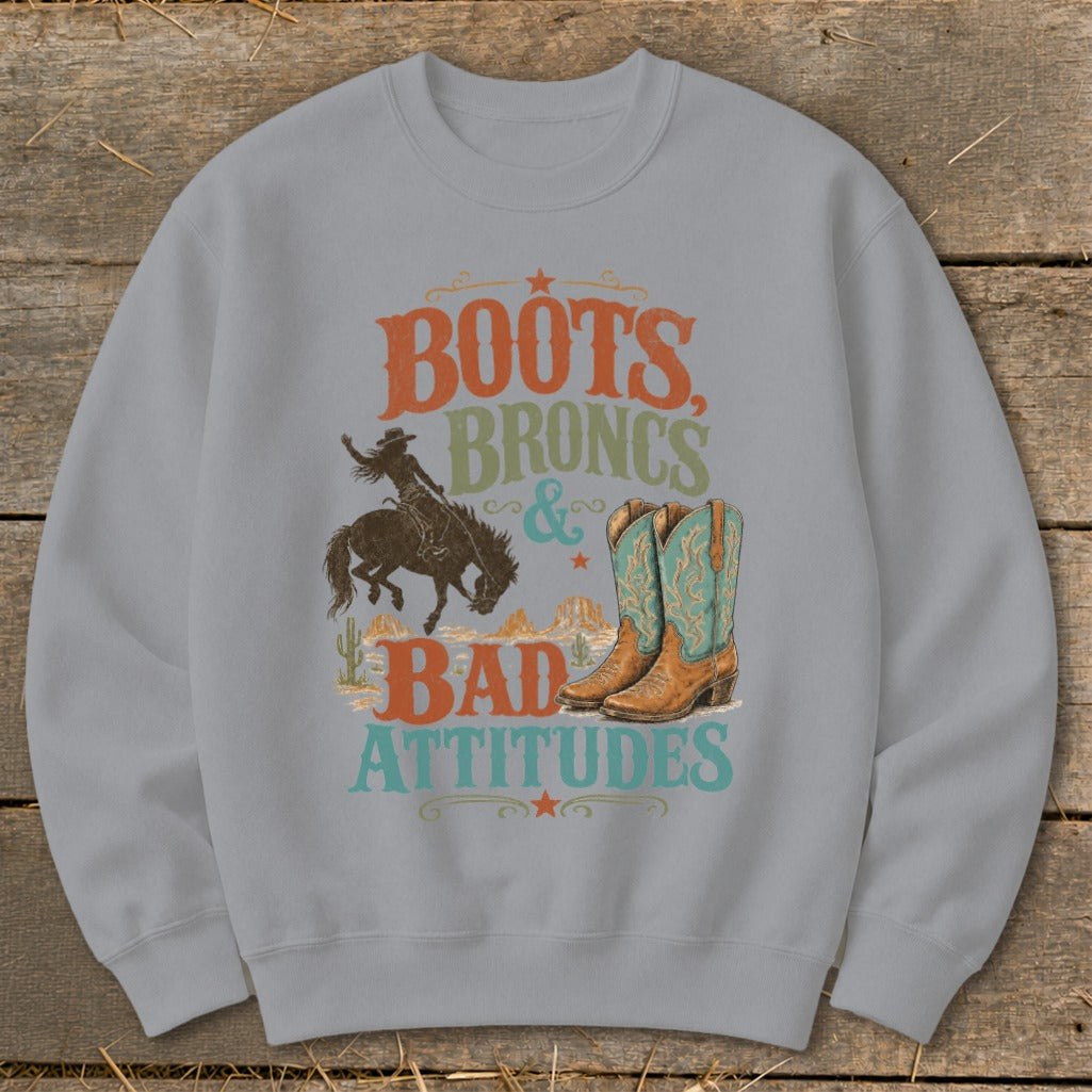Crewneck sweatshirt with "Boots, Broncs & Bad Attitudes" text, cowboy, and boots graphic.