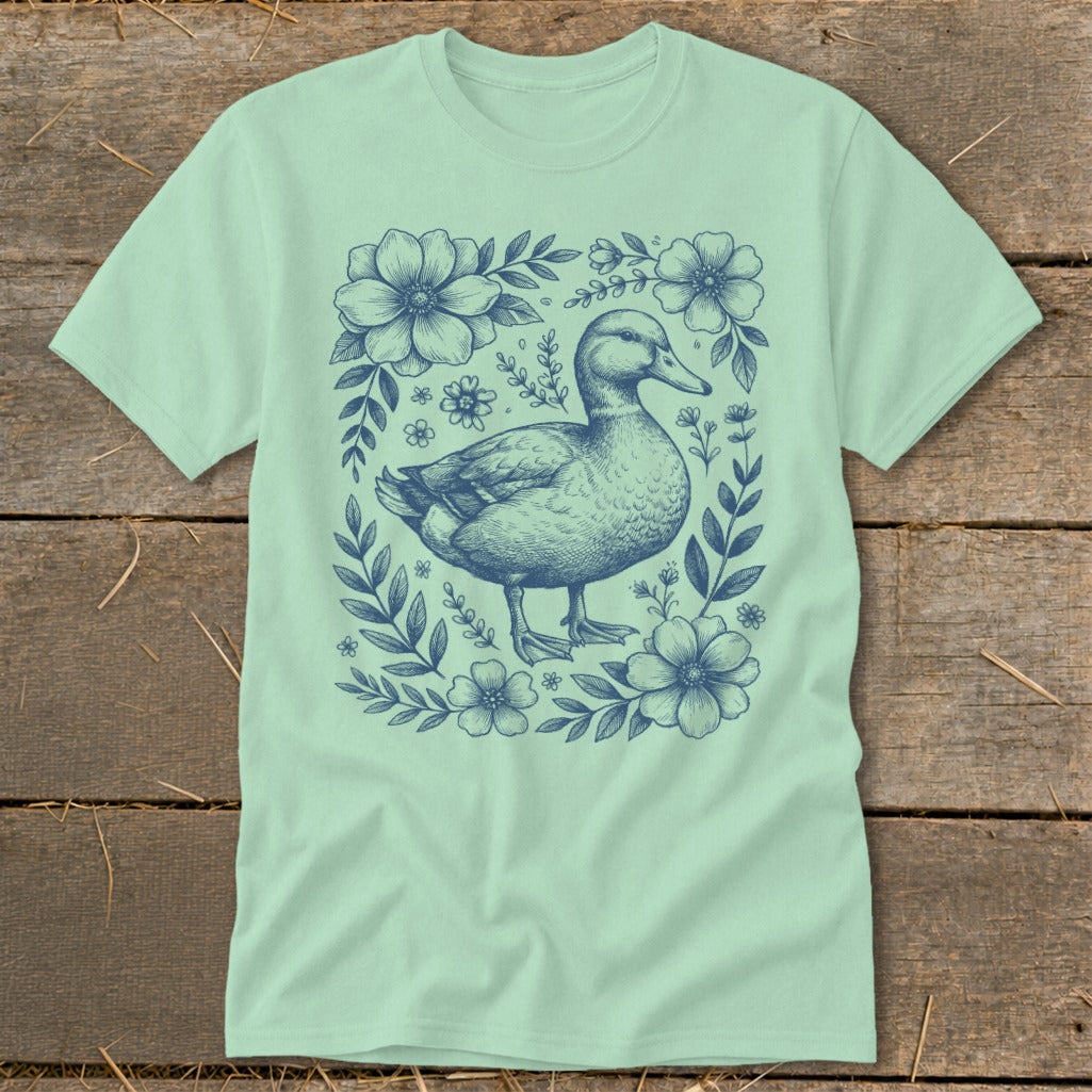 Light green t-shirt with a navy blue duck illustration surrounded by flowers.