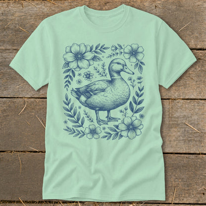 Light green t-shirt with a navy blue duck illustration surrounded by flowers.