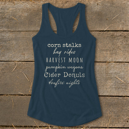 Navy tank top with text listing fall activities: corn stalks, hay rides, harvest moon, pumpkin wagons, cider donuts, bonfire nights.