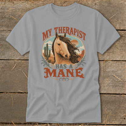T-shirt with "My therapist has a mane" text and horse illustration in desert landscape.