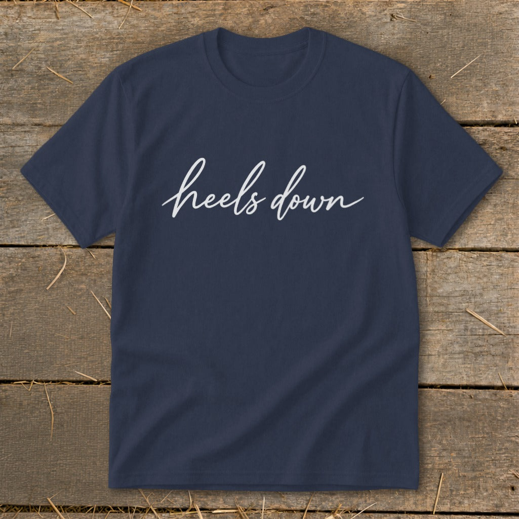 Navy t-shirt with white cursive text "heels down" on wooden background.
