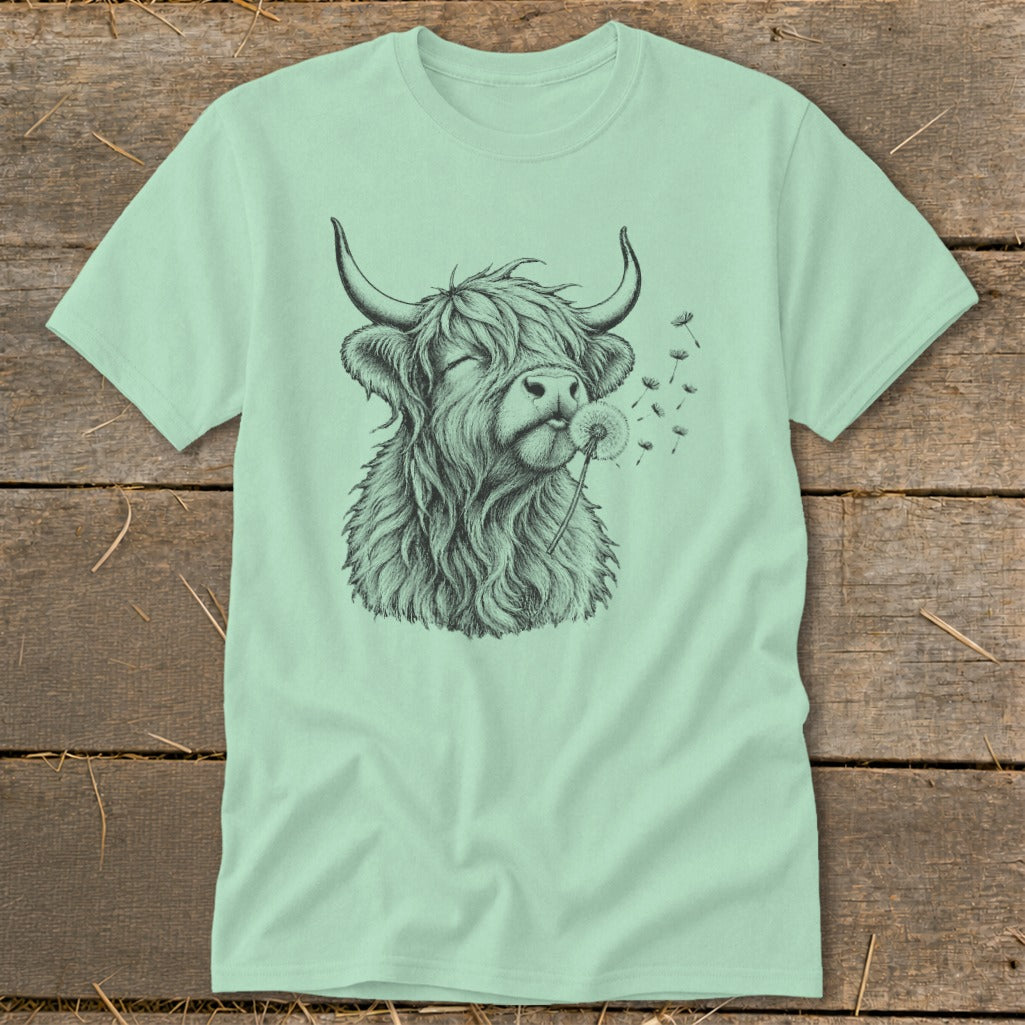 Light green t-shirt with a sketch of a Highland cow blowing a dandelion.