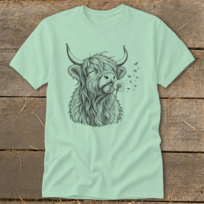 Light green t-shirt with a sketch of a Highland cow blowing a dandelion.