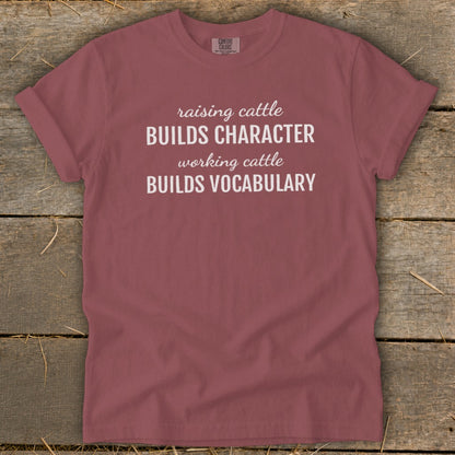 Maroon t-shirt with white text "Raising cattle BUILDS CHARACTER working cattle BUILDS VOCABULARY".