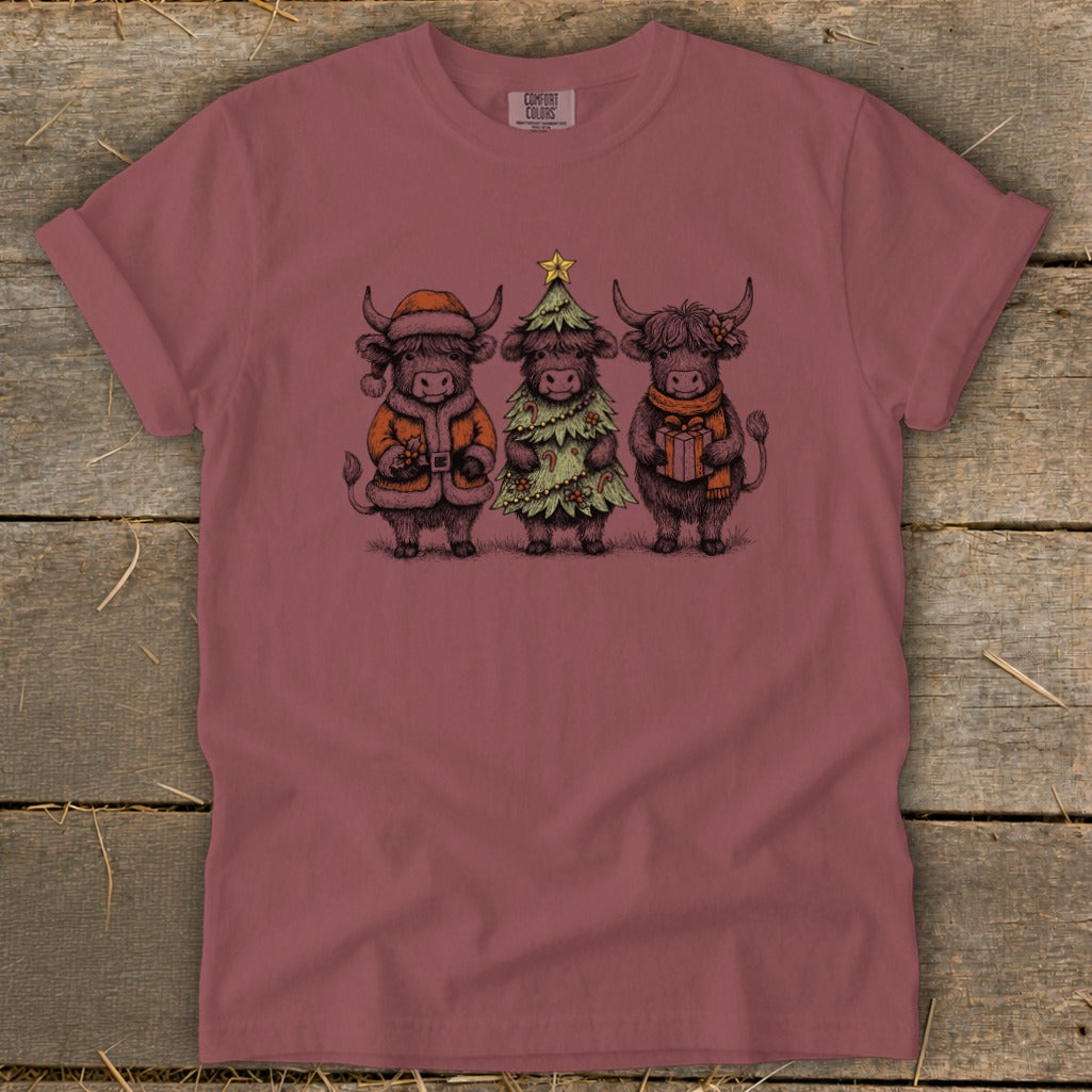 Three Highland cows dressed for Christmas: one in Santa suit, one as a tree, one with gift.