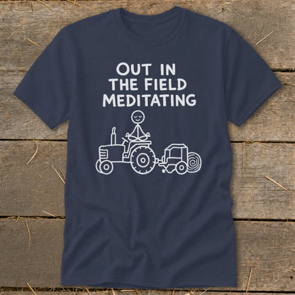 Navy t-shirt with white text "OUT IN THE FIELD MEDITATING" and stick figure on a tractor.