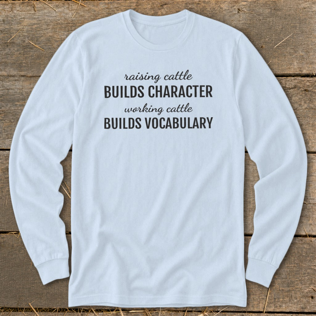 Light blue long-sleeve shirt with text "raising cattle BUILDS CHARACTER working cattle BUILDS VOCABULARY".