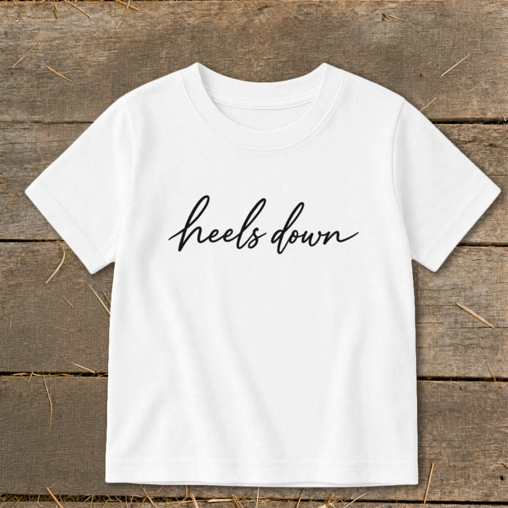 White t-shirt with black cursive text "heels down" on the chest.