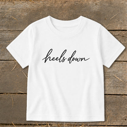 White t-shirt with black cursive text "heels down" on the chest.