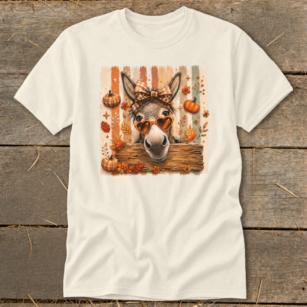 Donkey with heart sunglasses and plaid bow peeking over wooden fence, surrounded by pumpkins.