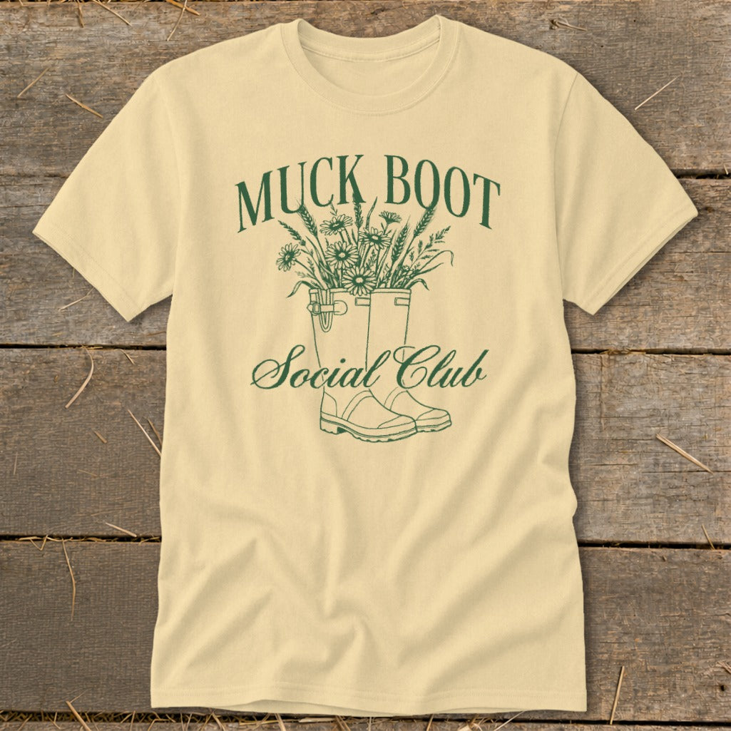 Cream t-shirt with green Muck Boot Social Club graphic of boots and flowers.