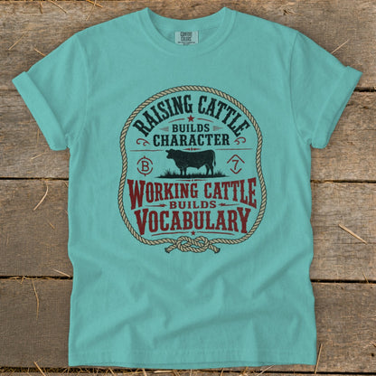 Teal t-shirt with rope border and text: Raising Cattle Builds Character, Working Cattle Builds Vocabulary.