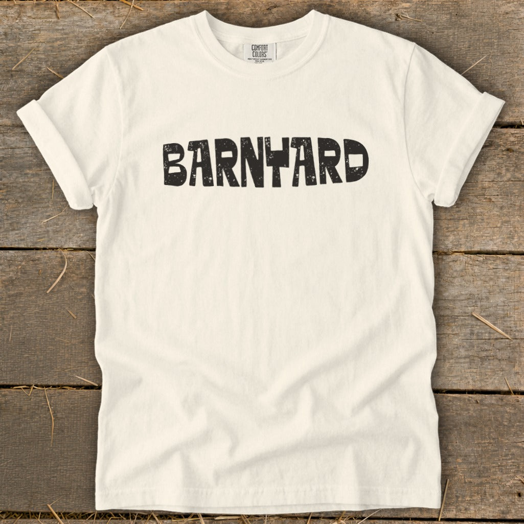 Off-white crewneck t-shirt featuring the black distressed text BARNYARD centered across the chest, laid on a rustic wooden surface.