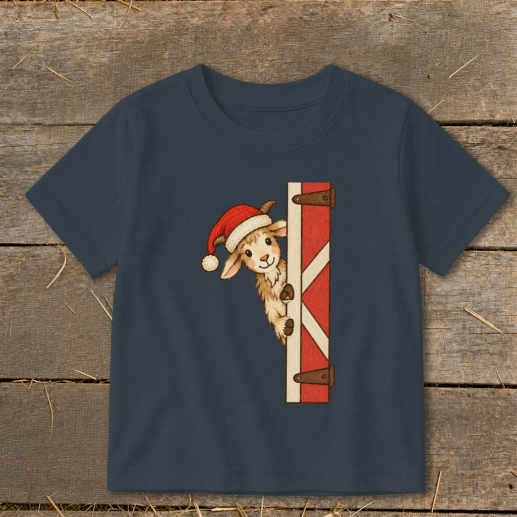 Navy t-shirt with a cartoon goat wearing a Santa hat peeking around a barn door.