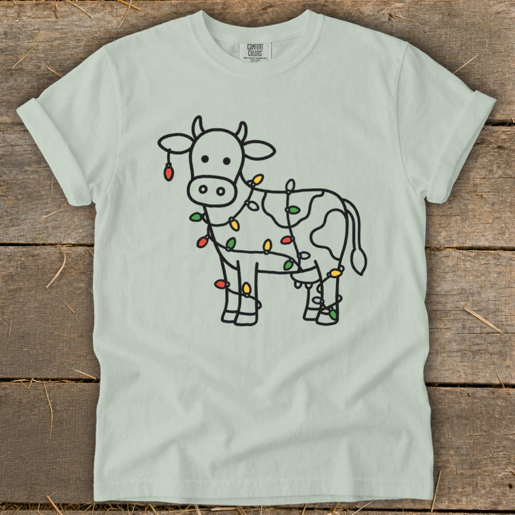 Light blue t-shirt with black outline drawing of a cow wrapped in colorful Christmas lights.