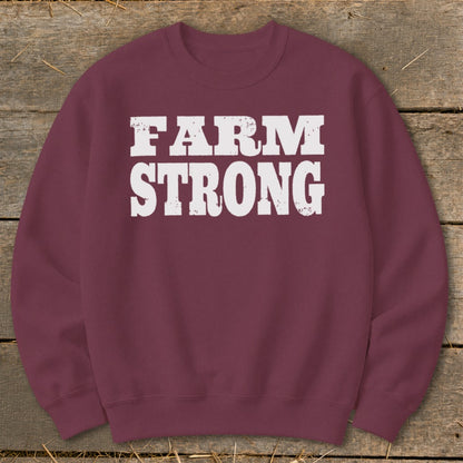 Maroon crewneck sweatshirt featuring the distressed white text FARM STRONG centered on the chest, laid flat on a rustic wooden background.