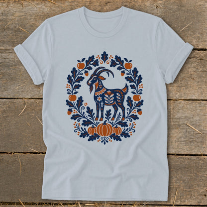 A light blue t-shirt displays an autumn-themed folk art graphic of a goat framed by leaves, acorns, and pumpkins.