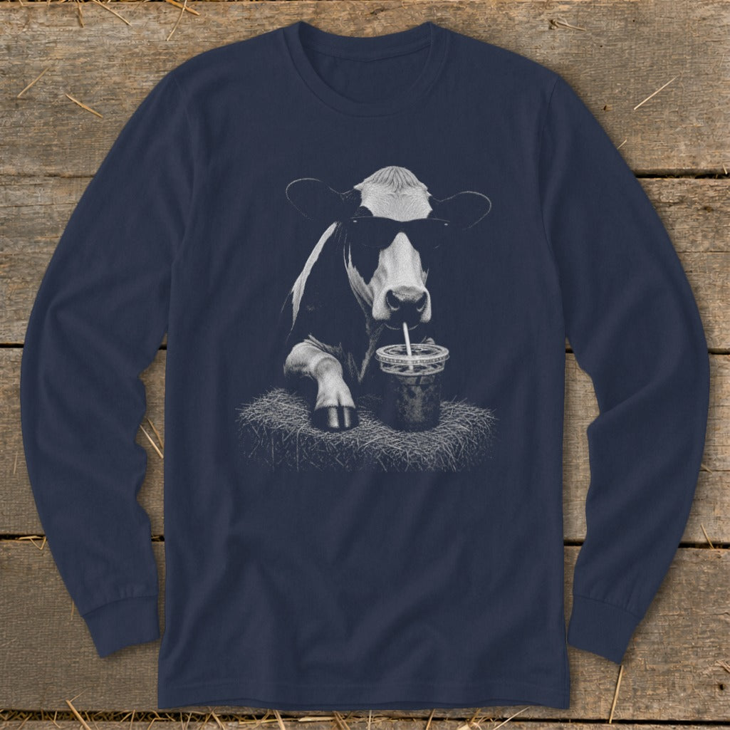 Cow with sunglasses drinking from a straw on a bale of hay.