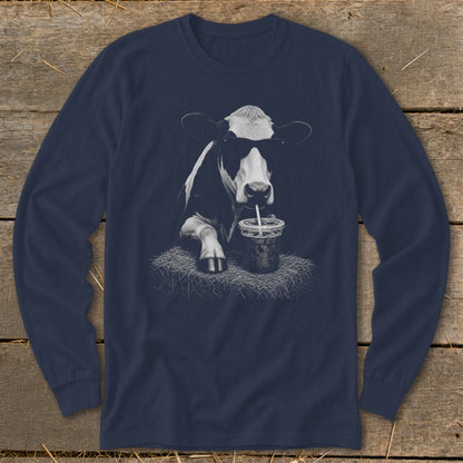 Cow with sunglasses drinking from a straw on a bale of hay.