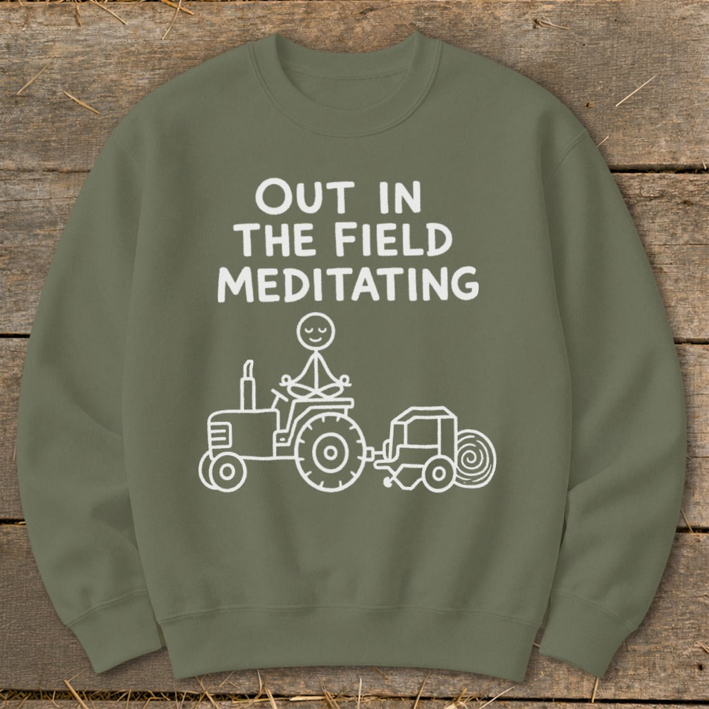 Olive green sweatshirt with white text "OUT IN THE FIELD MEDITATING" and a stick figure meditating on a tractor.