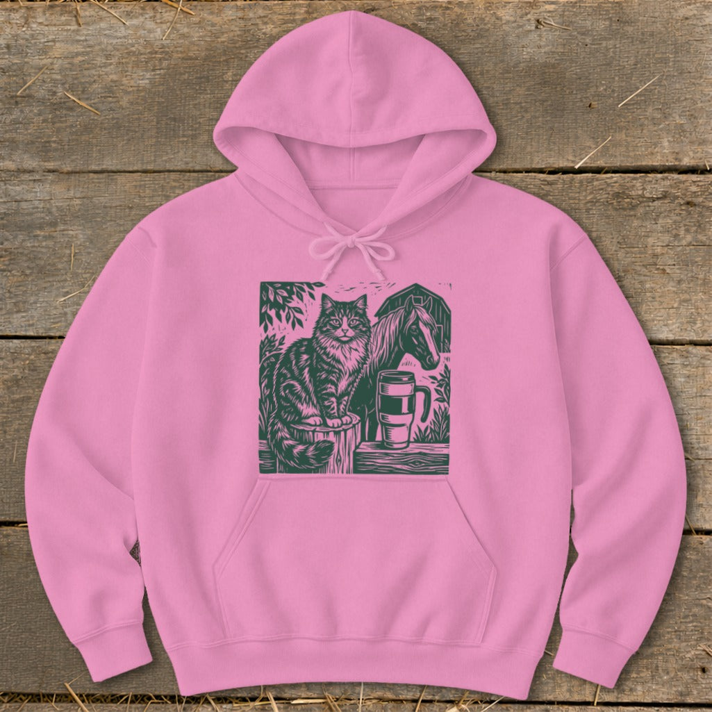 Pink hoodie with linocut print of a cat, horse, and mug on a wooden surface.