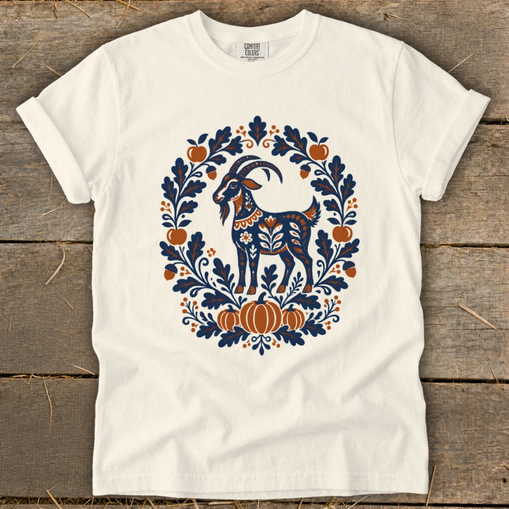 A cream-colored crewneck t-shirt featuring a folk-art goat illustration surrounded by an autumn wreath of pumpkins, leaves, and acorns.