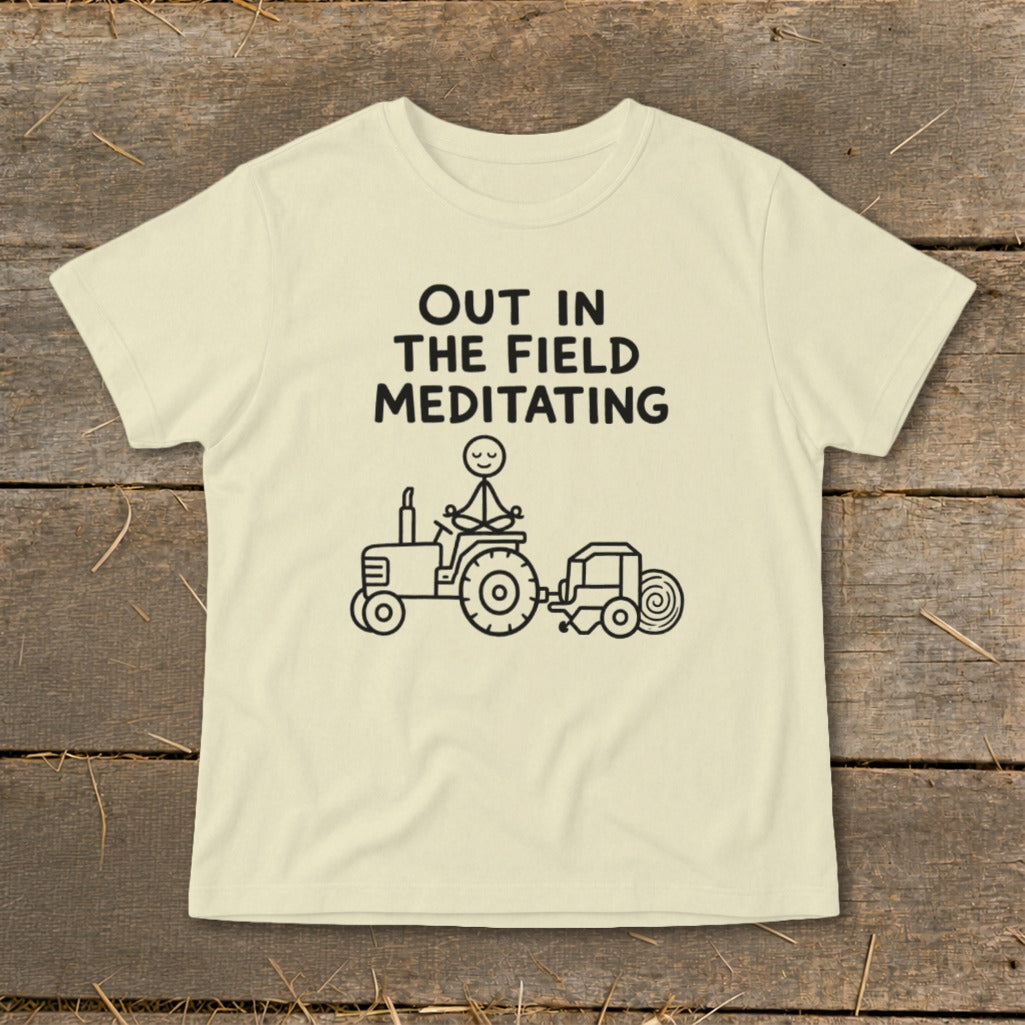 T-shirt with text "OUT IN THE FIELD MEDITATING" and drawing of stick figure meditating on tractor.