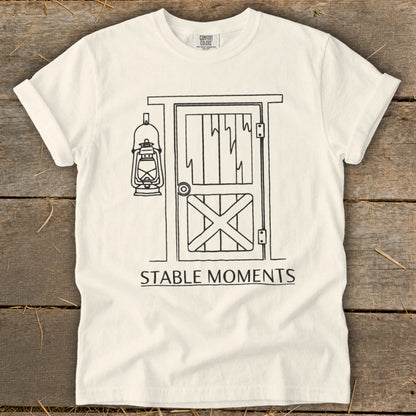 White t-shirt with a black line drawing of a stable door and a lantern, text "STABLE MOMENTS".