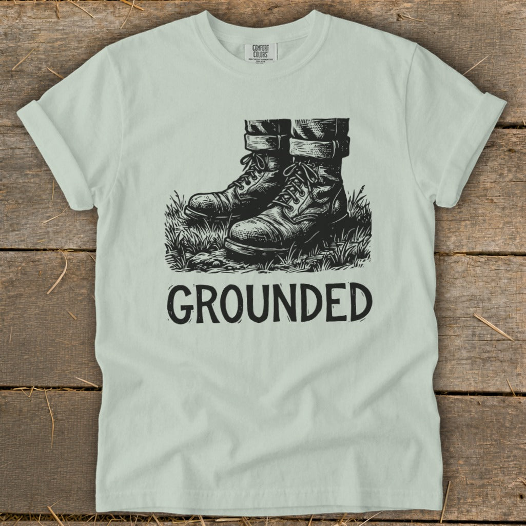 Light mint t-shirt with sketch of boots in grass and text "GROUNDED."