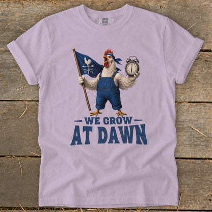 Light purple t-shirt with chicken graphic holding flag and alarm clock, text "We Grow At Dawn."
