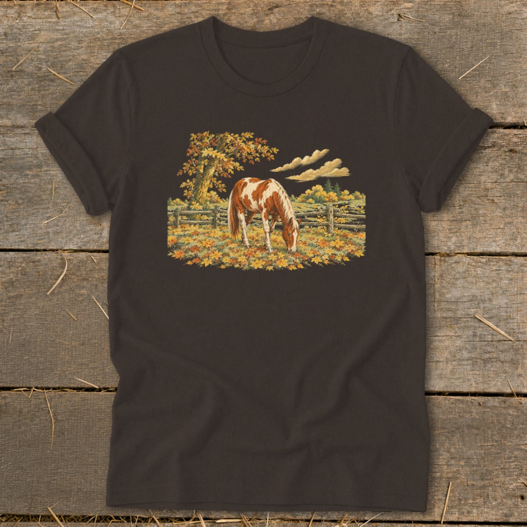 Brown and white horse grazing in autumn pasture with fallen leaves and wooden fence.