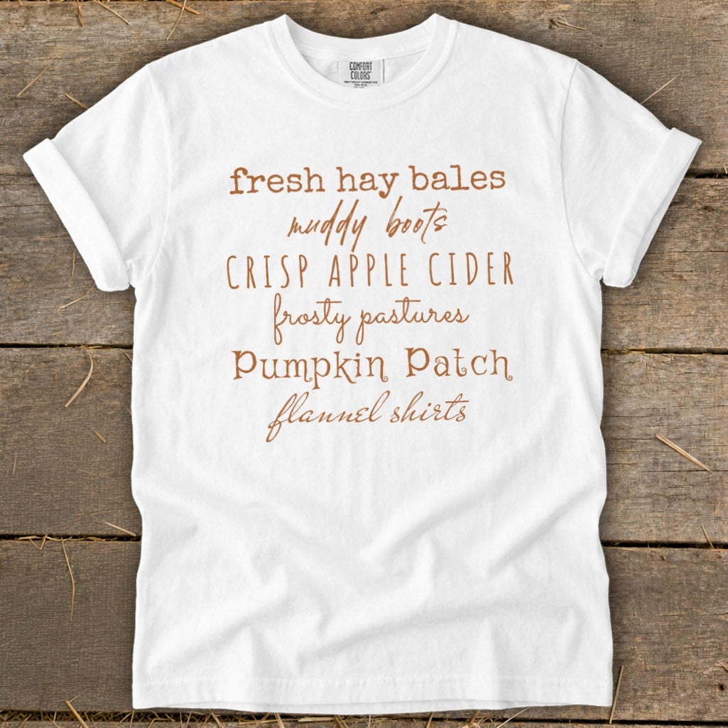 White t-shirt with text listing fall themes: fresh hay bales, muddy boots, crisp apple cider, frosty pastures, pumpkin patch, flannel shirts.