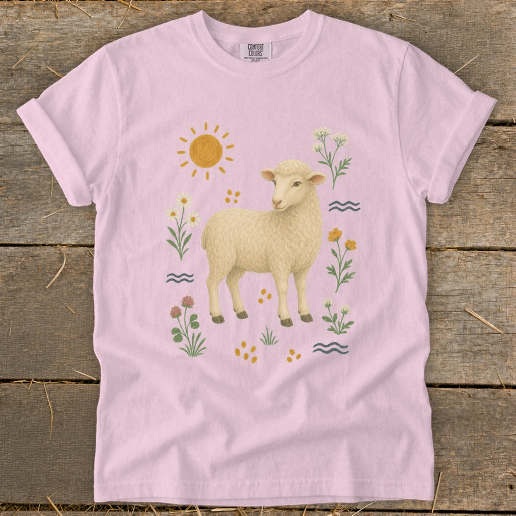 Pink t-shirt with a cream sheep graphic surrounded by sun, flowers, and wavy lines.