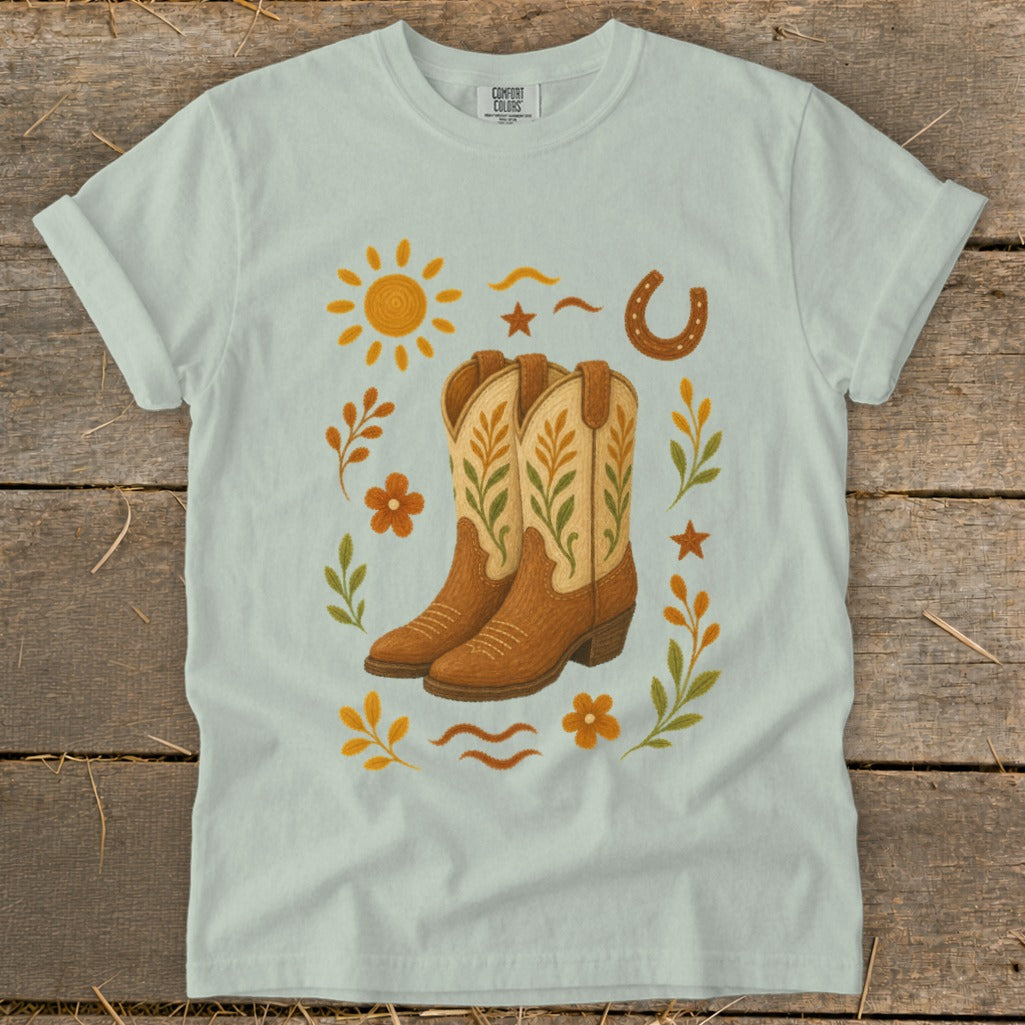 Light blue t-shirt featuring cowboy boots, sun, horseshoe, and floral accents.