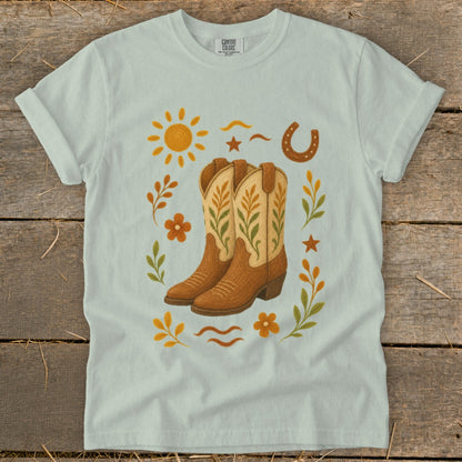 Light blue t-shirt featuring cowboy boots, sun, horseshoe, and floral accents.