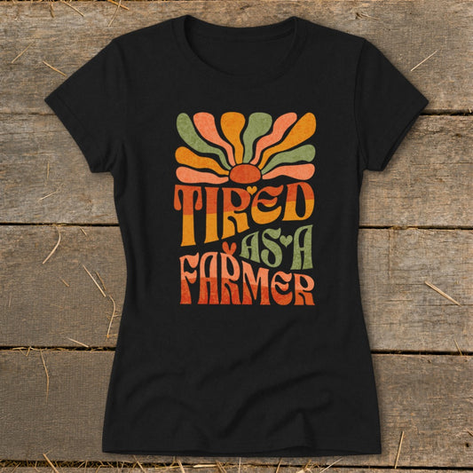 Black t-shirt with retro graphic text "Tired as a Farmer" and a sunburst.