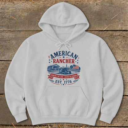 White hoodie with "American Rancher" design featuring a tractor, barn, and flag.