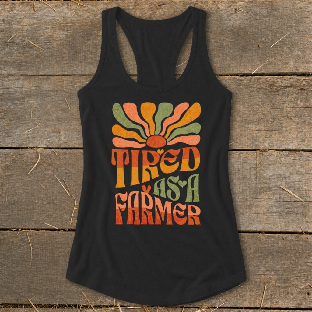 Black tank top with retro graphic reading "Tired As A Farmer" and a sunburst.