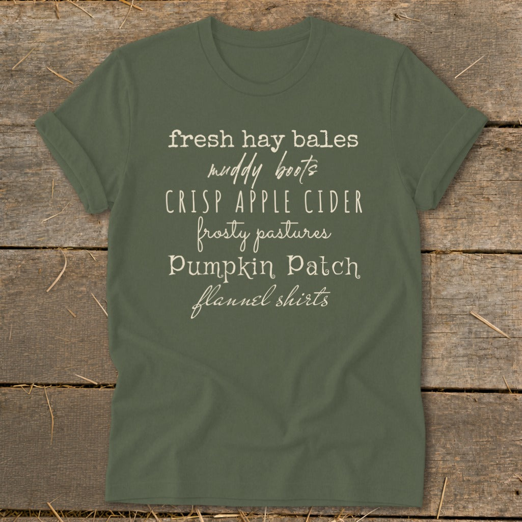 Olive green t-shirt with "fresh hay bales, muddy boots, crisp apple cider, frosty pastures, pumpkin patch, flannel shirts" text.