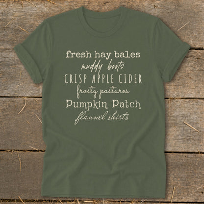 Olive green t-shirt with "fresh hay bales, muddy boots, crisp apple cider, frosty pastures, pumpkin patch, flannel shirts" text.