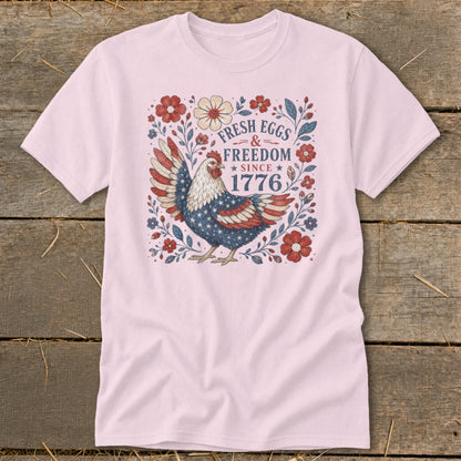 Pink t-shirt with a chicken design featuring "Fresh Eggs & Freedom Since 1776".