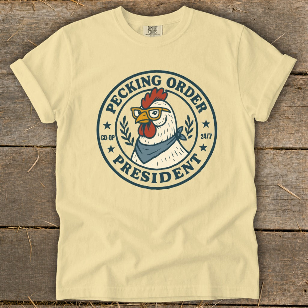 T-shirt with a circular graphic featuring a chicken wearing glasses and a bandana, reading "Pecking Order President".