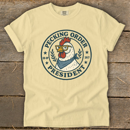 T-shirt with a circular graphic featuring a chicken wearing glasses and a bandana, reading "Pecking Order President".