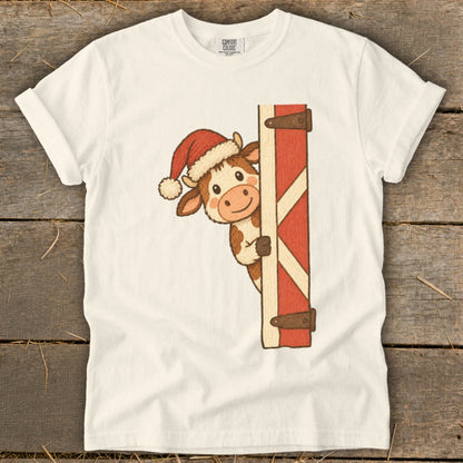 Cow wearing Santa hat peeking from behind a red barn door.