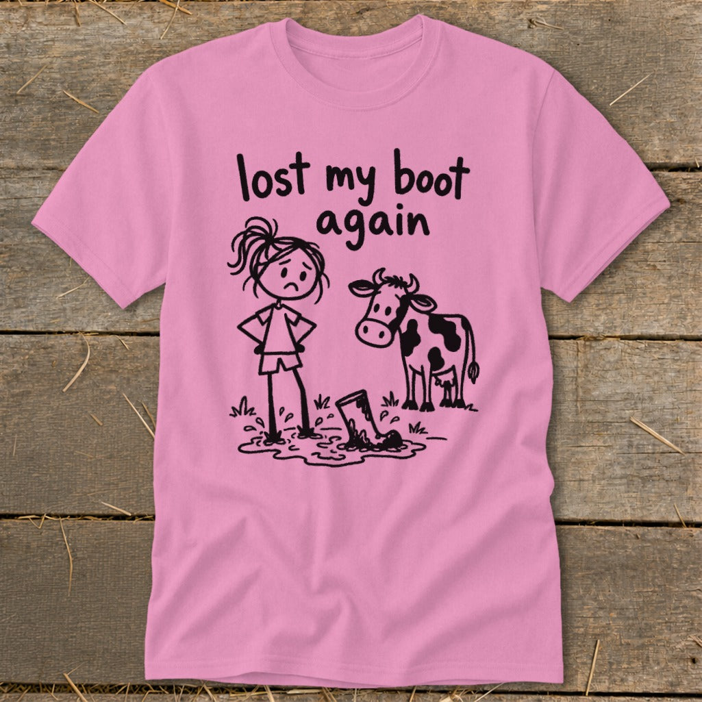A pink t-shirt featuring a cartoon of a sad girl standing in mud next to a cow, with the text "lost my boot again".