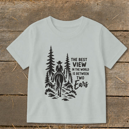 A light gray children's t-shirt features a black graphic of a horse and rider surrounded by trees and the text The Best View in the World Is Between Two Ears.