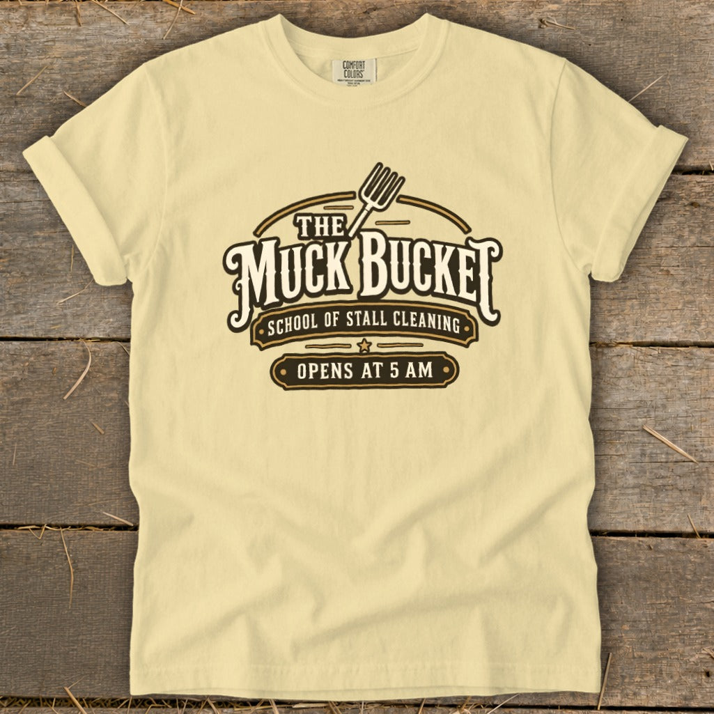 Pale yellow t-shirt with "The Muck Bucket School of Stall Cleaning Opens at 5 AM" graphic.
