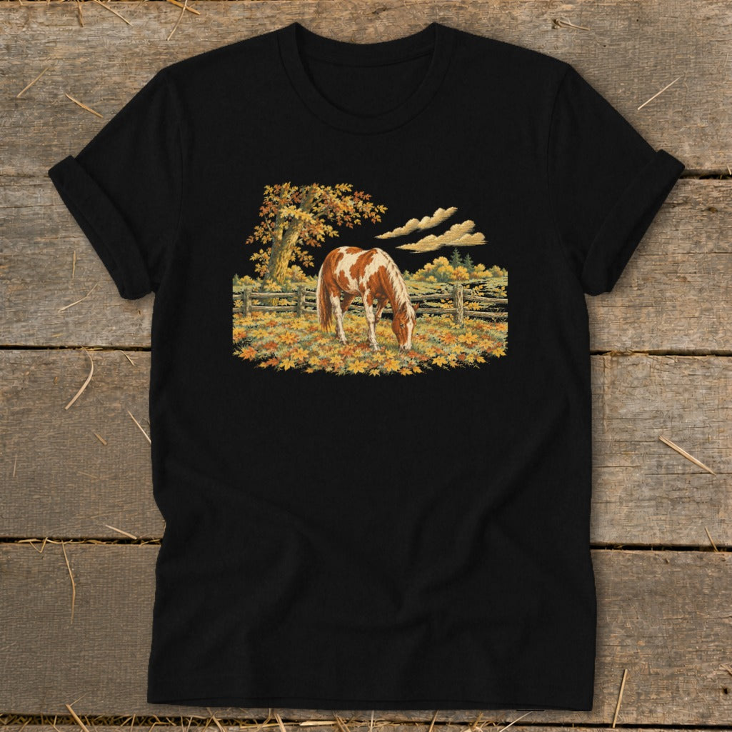 Black t-shirt with a graphic of a pinto horse grazing in a field of autumn leaves.