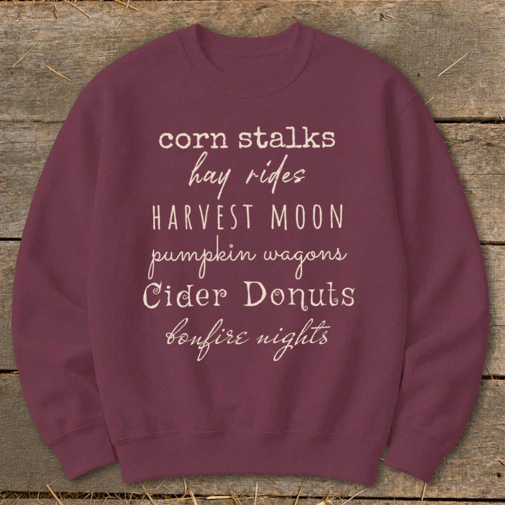 Maroon sweatshirt with white text listing "corn stalks, hay rides, HARVEST MOON, pumpkin wagons, Cider Donuts, bonfire nights".